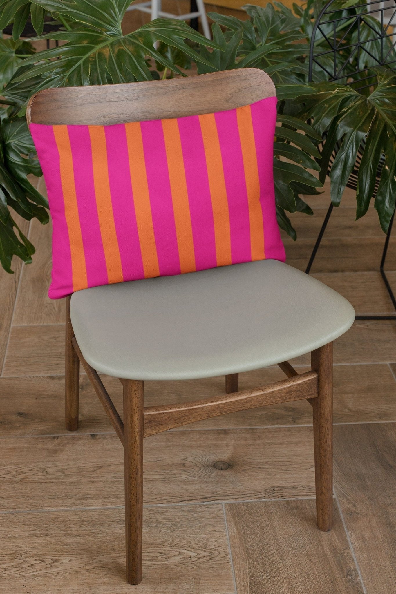 orange and pink outdoor lumbar pillow on chair with plants